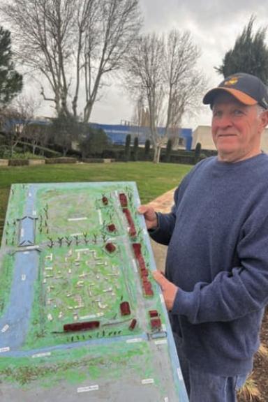 Un homme tient une maquette dans ses mains, celle du musée départemental. Il se trouve à l'extérieur, dans un champ près du musée.