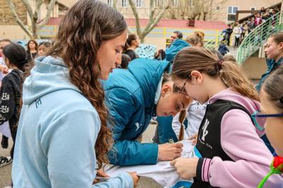 Une joueuse de l'Olympique de Marseille signe un maillot pour une jeune élève lors d'une rencontre dans la cour du collège, entourée de camarades enthousiastes. - Agrandir l'image 8 sur 16, fenêtre modale