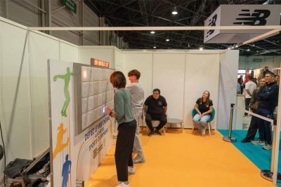 Stand interactif lors d’un salon sportif avec deux personnes utilisant un mur lumineux pour un défi de réflexes, sous une structure blanche avec sol orange et bleu. - Agrandir l'image 1 sur 12, fenêtre modale