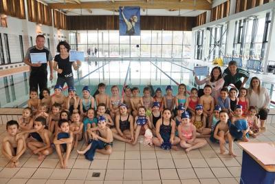Enfants en maillot de bain près d'une piscine intérieure, lors d'une remise de diplômes de natation. Les enfants sont assis, entourés des moniteurs. - Agrandir l'image 6 sur 8, fenêtre modale