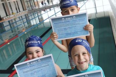 Trois enfants en bonnet de bain, debouts, tenant un certificat de réussite pass nautique au bord d’une piscine intérieure. - Agrandir l'image 1 sur 8, fenêtre modale