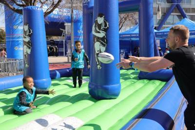 des enfants dans une structure gonflable de rugby s'apprêtent à recevoir un ballon de rugby envoyé par un adulte - Agrandir l'image 2 sur 9, fenêtre modale