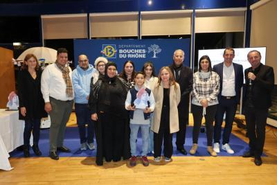 Groupe de participants réunis sur une scène avec un fond bleu « Département Bouches-du-Rhône », une personne au centre tenant un trophée coloré. - Agrandir l'image 3 sur 6, fenêtre modale