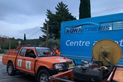 Deux véhicules orange du CCFF de Peypin sont stationnés devant le camion-piscine du Département. Un enrouleur avec tuyaux est visible sur la remorque. Arrière-plan : arbres, ciel nuageux, route et poteaux électriques. - Agrandir l'image 4 sur 5, fenêtre modale