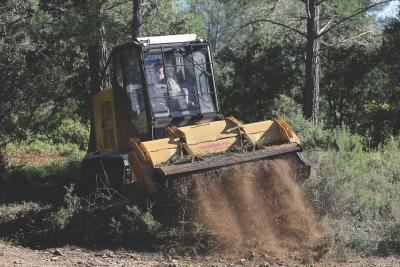 Engin forestier jaune et noir en action, projetant de la terre et des végétaux broyés sur un chemin dans une zone boisée. - Agrandir l'image 2 sur 6, fenêtre modale