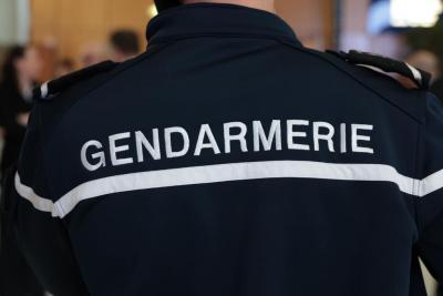 Un adulte en uniforme bleu foncé portant l’inscription “GENDARMERIE” est vu de dos. La scène est en intérieur, avec plusieurs silhouettes autour suggérant une réunion ou une rencontre interservices. L’atmosphère est officielle, il s'agissait de cérémonie des voeux au personnel des forces de l'ordre et de secours des Bouches-du-Rhône. - Agrandir l'image 4 sur 18, fenêtre modale