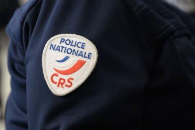 Un adulte en uniforme sombre est montré de près, centré sur la manche. Un écusson en forme de bouclier est cousu sur le bras, portant l’inscription “POLICE NATIONALE” en bleu et “CRS” en rouge, accompagnée de courbes tricolores bleu‑blanc‑rouge. L’environnement semble être un espace intérieur avec d’autres personnes en tenue professionnelle en arrière‑plan. On se trouve à la cérémonie des vœux au personnel des forces de l'ordre et de secours. - Agrandir l'image 16 sur 18, fenêtre modale