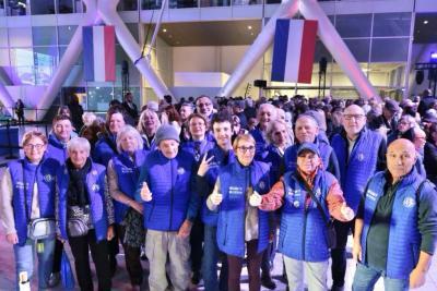 Groupe de personnes vêtues de gilets bleus posant ensemble devant une foule et des drapeaux français - Agrandir l'image 12 sur 20, fenêtre modale