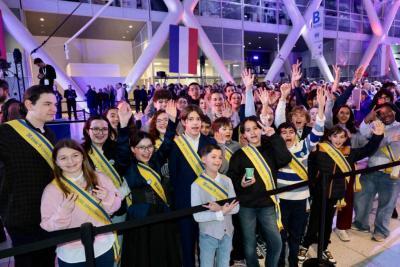 Groupe d’enfants et adolescents portant des écharpes officielles, rassemblés et saluant le public dans un hall événementiel - Agrandir l'image 14 sur 20, fenêtre modale