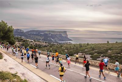 Groupe de coureurs participant au semi-marathon Marseille-Cassis sur une route côtière, avec vue sur la mer Méditerranée et les falaises de Cassis en arrière-plan. - Agrandir l'image 5 sur 12, fenêtre modale