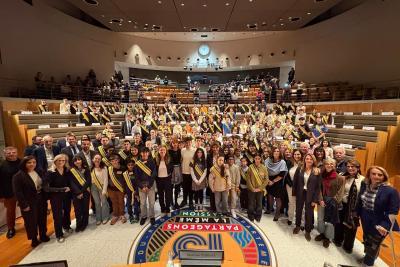 Large groupe d’adolescents et d’adultes rassemblés au centre d’un hémicycle. Beaucoup portent des écharpes officielles. On distingue le sol décoré, les gradins pleins et l’ambiance solennelle d’une photo collective. - Agrandir l'image 6 sur 6, fenêtre modale