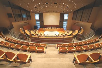 Grande salle de séance publique aménagée par Andrée Putman, avec des rangées de sièges en bois autour d'un espace central éclairé. La salle est très éclairée. - Agrandir l'image 1 sur 3, fenêtre modale