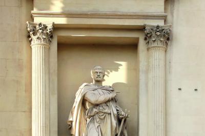 statue d'un homme paré d'une cape par dessus sa tunique et son pantalon, pointant son doigt droit dans une direction tandis que sa main gauche tient un petit trident - Agrandir l'image 2 sur 3, fenêtre modale