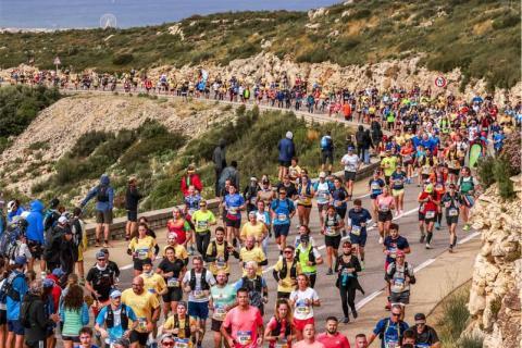 Grande foule de coureurs participant au semi-marathon Marseille-Cassis sur une route sinueuse bordée de rochers, avec vue sur la mer Méditerranée et les îles au loin.