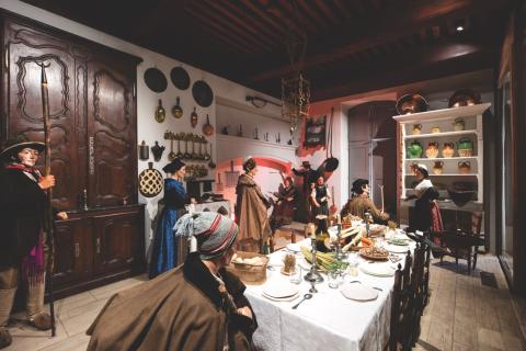 gros plan sur une reconstitution d'une salle à manger provençale avec des casseroles aux murs des placards et une grande tablée couverte de mets provençaux