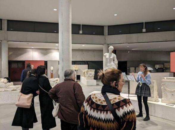 Groupe dans une des salles du Musée Arles Antique avec de nombreuses sculptures autour d'eux. Une personne est placée face à eux, elle est en train de faire une lecture dans le cadre des nuits de la lecture au Musée départemental Arles Antiques. - Agrandir l'image, fenêtre modale