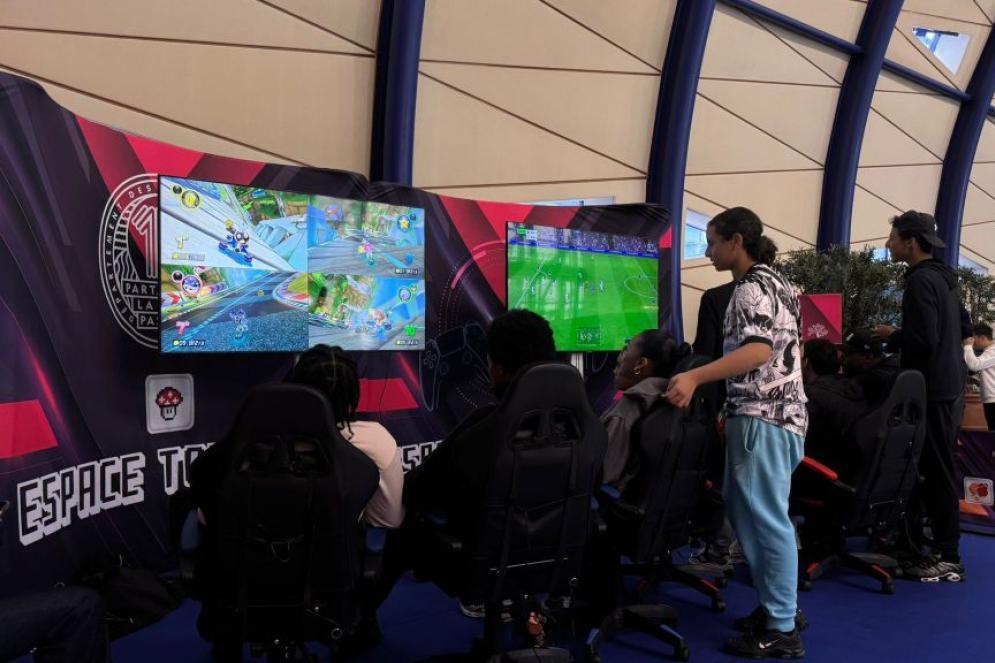 Lors du Mercredi sport et e-sport des Bouches-duRhône, plusieurs jeunes adultes jouent à Mario Kart et FIFA sur deux grands écrans dans un espace dédié au gaming. Assis dans des fauteuils de compétition, concentrés sur leurs manettes, ils sont entourés d’un décor avec l’inscription “Espace Tournoi E-sport” . L’ambiance est immersive, moderne et tournée vers le jeu vidéo compétitif.